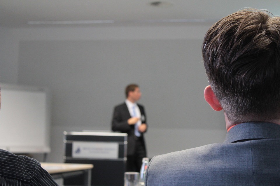 A blurred photo of a man in a black suit in front of an audience