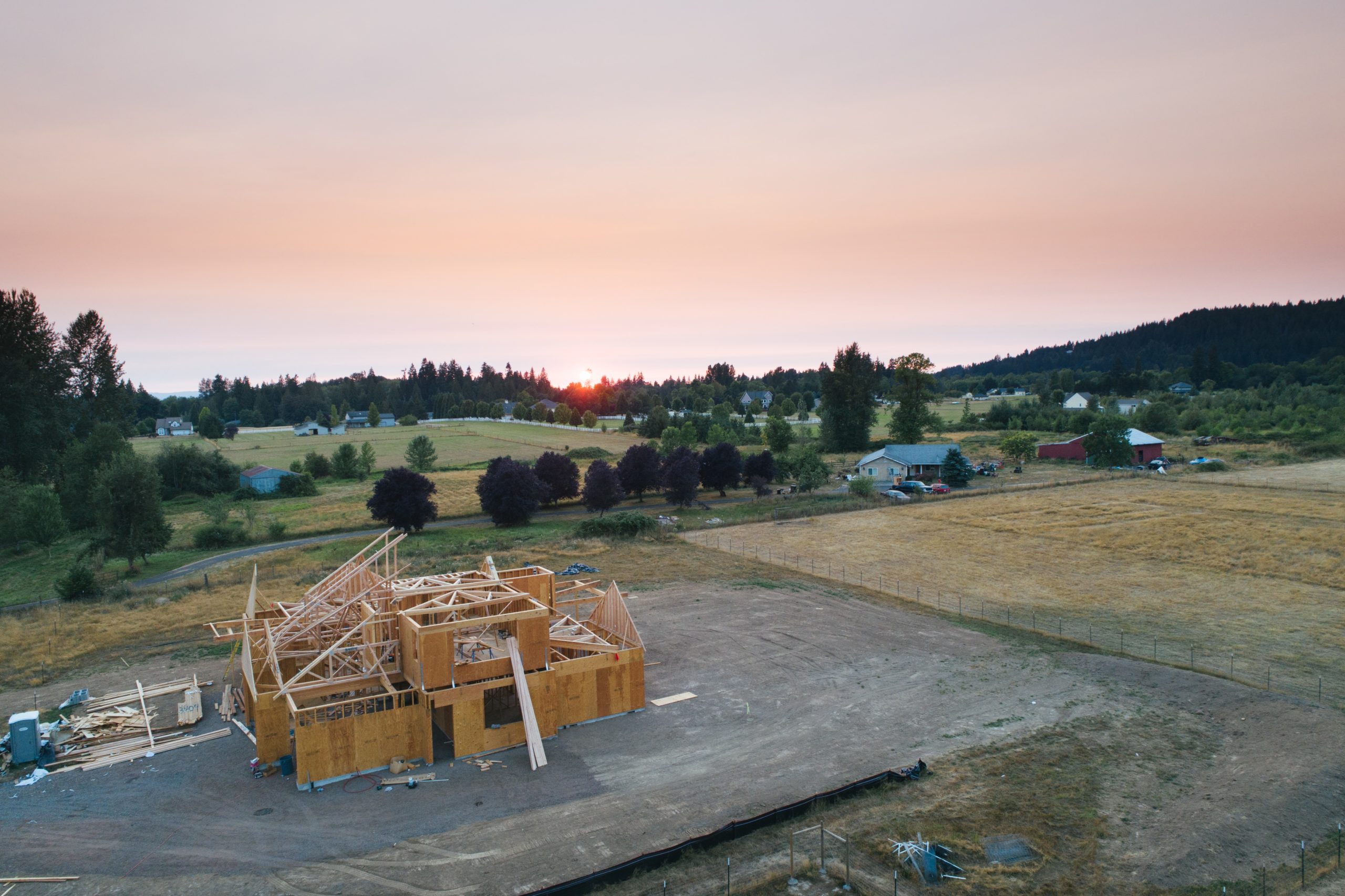 A property building site surrounded by fields and trees during sunset