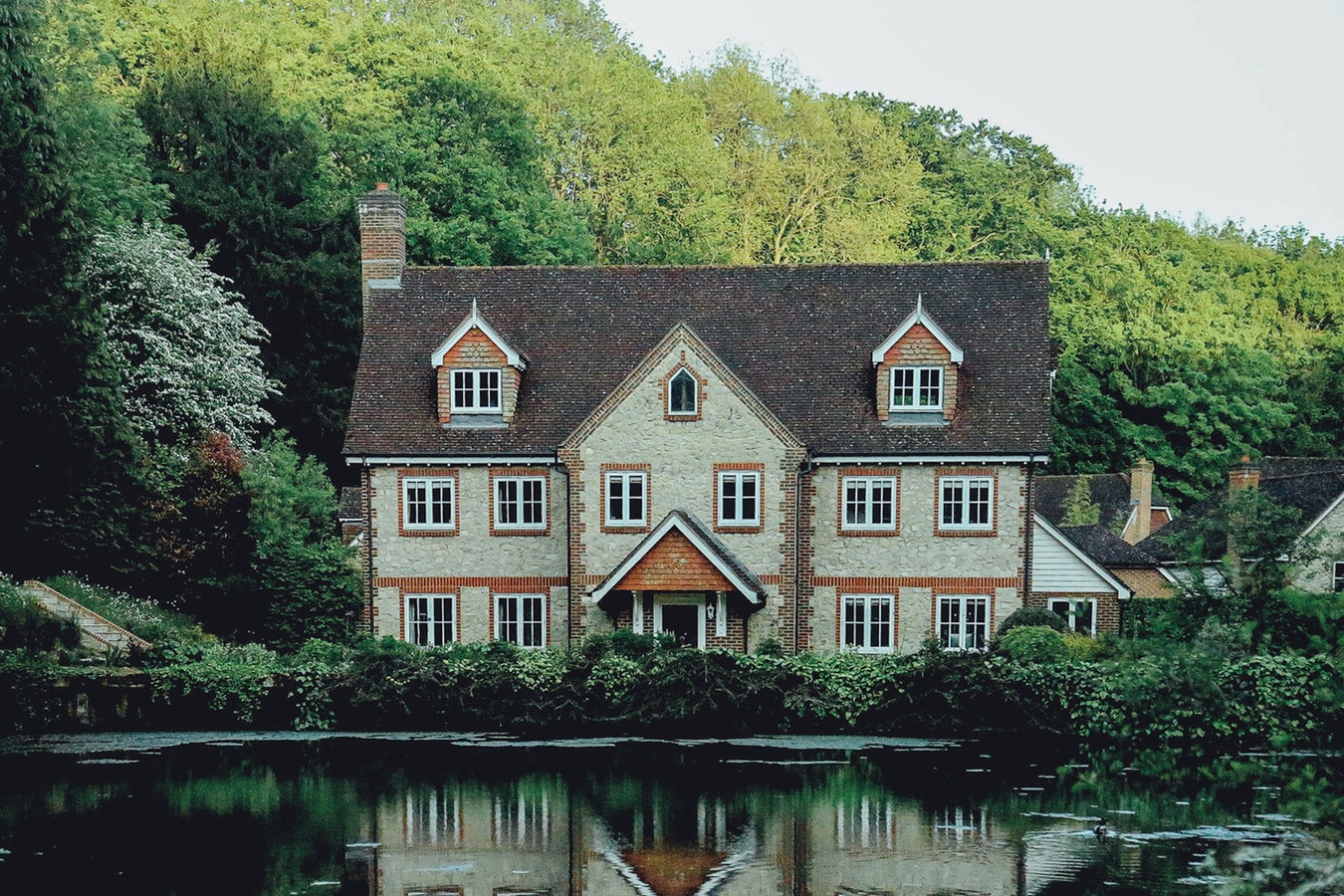 A brick house in front of a river surrounded by trees