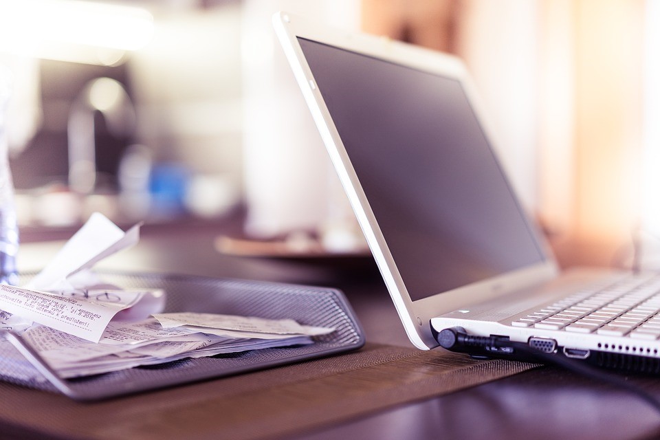 A laptop on a desk next to a stack of receipts