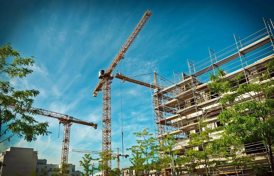 A building surrounded by scaffolding, cranes and trees