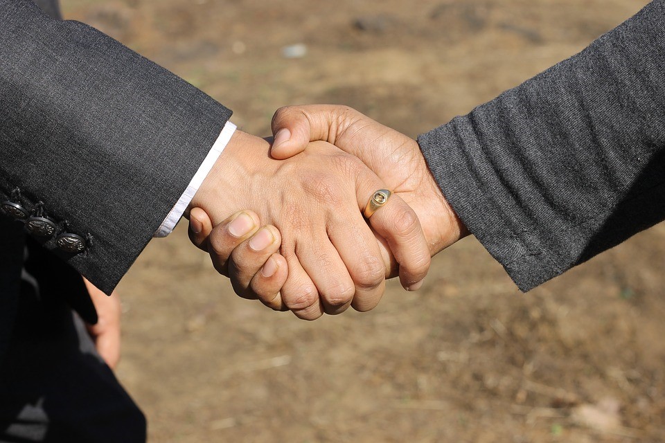 Two people shaking hands wearing black suits