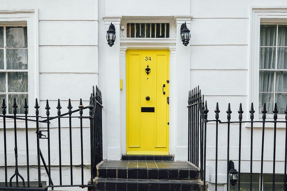 Street view of a house with a yellow door and black gates