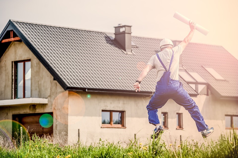 Builder in blue overalls jumping outside of house