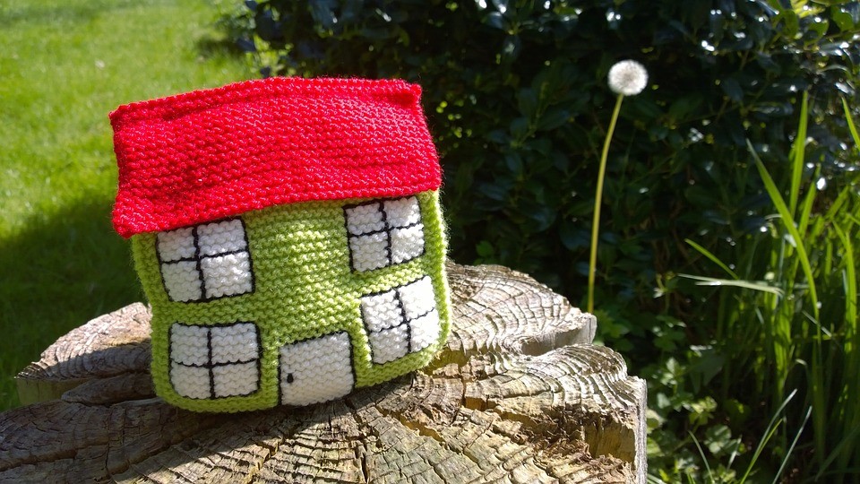 Small knitted house on top of a log in a garden
