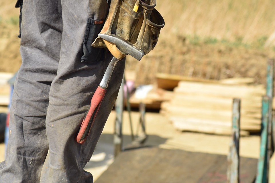 Construction worker wearing baggy trousers holding a hammer