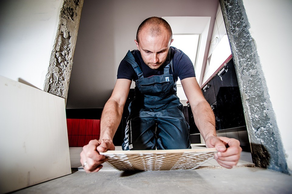 Person wearing overalls laying tiled floor between a doorway