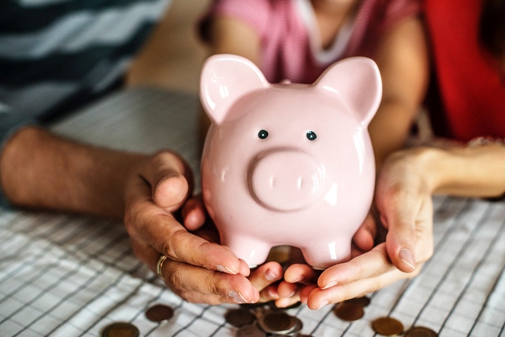 Three people holding a pink piggybank